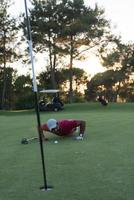 golf speler blazen bal in gat met zonsondergang in achtergrond foto