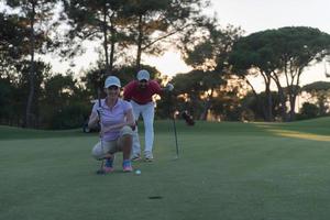 paar Aan golf Cursus Bij zonsondergang foto