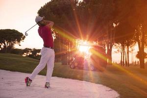 golfspeler raken een zand bunker schot Aan zonsondergang foto