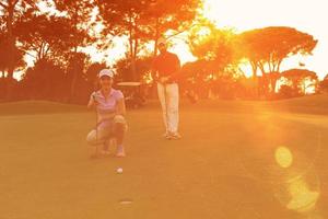 paar Aan golf Cursus Bij zonsondergang foto