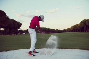 golfspeler raken een zand bunker schot Aan zonsondergang foto