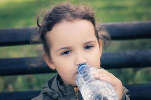 weinig meisje drinken water van plastic fles. foto