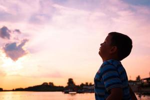 klein jongen tegen de lucht Bij zonsondergang. foto