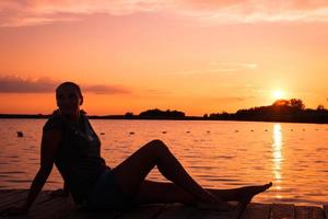 zorgeloos vrouw ontspannende Aan pier Bij zonsondergang. foto