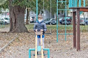 klein jongen met beschermend gezicht masker spelen alleen in de park. foto