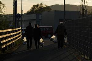 silhouet van drie mensen draag- een boodschappen doen Tassen Bij zonsondergang. foto