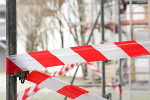 Aan een bouw plaats, een rood en wit plastic barrière plakband blijft hangen Aan een steiger foto