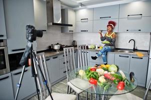 Afrikaanse Amerikaans vrouw filmen haar blog uitzending over gezond voedsel Bij huis keuken. ze houden bord met salade. foto