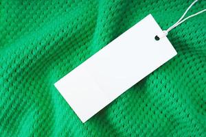 wit blanco rechthoekig kleding label Aan groen gebreid kleding stof achtergrond. winkelen, uitverkoop, korting mockup foto