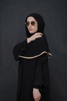 jong moslim in traditioneel kleren of abaya en zonnebril poseren in voorkant van zwart schoolbord foto