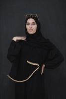 jong moslim in traditioneel kleren of abaya en zonnebril poseren in voorkant van zwart schoolbord foto