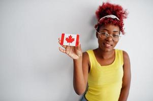 Afrikaanse Amerikaans vrouw met afro haar, slijtage geel singlet en bril, houden Canada vlag geïsoleerd Aan wit achtergrond. foto