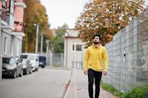 stedelijk jong hipster Indisch Mens in een modieus geel trui. koel zuiden Aziatisch vent slijtage capuchon wandelen Aan vallen straat. foto