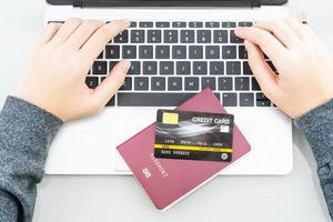 vrouw handen typen Aan laptop computer met paspoort en credit kaart foto