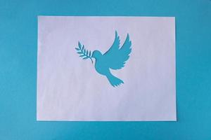 een duif stencil met een takje, besnoeiing uit van wit papier Aan een blauw achtergrond voor wereld vrede dag. wereld wetenschap dag voor vrede en ontwikkeling foto
