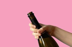 een vrouw hand- Holding een Open fles van Champagne Aan een roze achtergrond foto