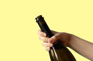 een vrouw hand- Holding een Open fles van Champagne Aan een geel achtergrond.vakantie concept. plaats voor uw tekst foto