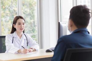 Aziatisch professioneel vrouw dokter wie draagt medisch jas praat met een Mens geduldig naar raadplegen en stel voor gezondheidszorg informatie naar hem. foto