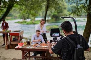 een professioneel uitgerust cameraman is filmen een groep van mensen hebben avondeten door de rivier. foto