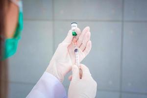 dokter is gebruik makend van injectiespuit naar zuigen vaccin coronavirus vaccin van fles terwijl haar handen slijtage rubber handschoenen. foto