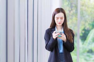 Aziatisch werken vrouw toepassingen smartphone naar babbelen met iemand in digitalisering concept. foto