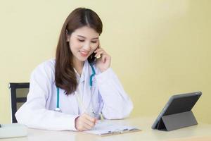 een mooi vrouw dokter telefoontje telefoon en schrijven naar controleren symptoom foto