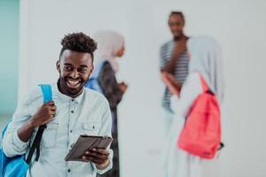 Universiteit levensstijl knap jong leerling Mens Holding een tablet computer en glimlachen terwijl staand tegen Universiteit met zijn vrienden hebben een team vergadering in de achtergrond. hoge kwaliteit foto