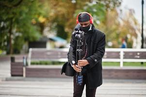 jong professioneel Afrikaanse Amerikaans videograaf Holding professioneel camera met pro apparatuur. afro cameraman vervelend zwart Duraq en gezicht beschermen masker, maken een videos. foto