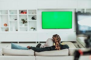 Afrikaanse paar zittend Aan sofa aan het kijken TV samen chroma groen scherm vrouw vervelend Islamitisch hijab kleren foto