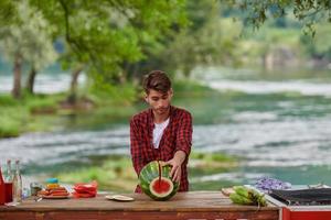 Mens snijdend sappig watermeloen gedurende buitenshuis Frans avondeten partij foto