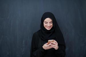 jong moslim zakenvrouw in traditioneel kleren of abaya gebruik makend van smartphone foto