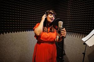 jong Aziatisch zanger met microfoon opname lied in Vermelding muziek- studio. foto