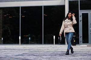 modieus Afrikaanse Amerikaans vrouw slijtage baret en jas met handtas poseren buitenshuis. foto