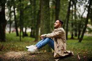 elegant Koeweit Mens Bij loopgraaf jas zitten Aan boom Bij hout. foto