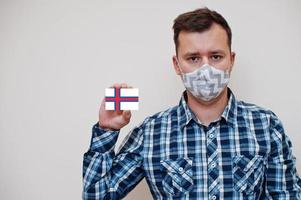 Mens in geruit overhemd tonen Faeröer eilanden vlag kaart in hand, slijtage beschermen masker geïsoleerd Aan wit achtergrond. Europa landen coronavirus concept. foto