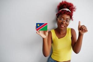 Afrikaanse vrouw met afro haar, slijtage geel singlet en bril, houden Namibië vlag geïsoleerd Aan wit achtergrond, tonen duim omhoog. foto