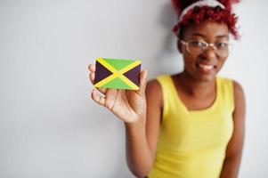 Afrikaanse Amerikaans vrouw met afro haar, slijtage geel singlet en bril, houden Jamaica vlag geïsoleerd Aan wit achtergrond. foto