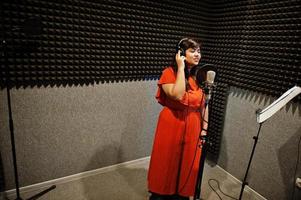 jong Aziatisch zanger met microfoon opname lied in Vermelding muziek- studio. foto