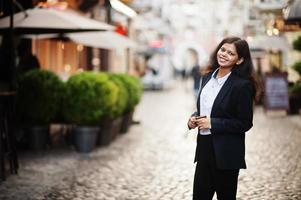 prachtig Indisch vrouw slijtage formeel poseren Bij straat met mobiel telefoon Bij handen. foto