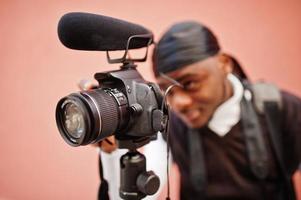 jong professioneel Afrikaanse Amerikaans videograaf Holding professioneel camera met pro apparatuur. afro cameraman vervelend zwart Duraq maken een videos. foto