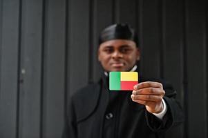 Afrikaanse Mens slijtage zwart durag houden Benin vlag Bij hand- geïsoleerd donker achtergrond. foto