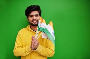 stedelijk jong hipster Indisch Mens in een modieus geel sweater houden vlaggen van Indië in handen. koel zuiden Aziatisch vent slijtage capuchon geïsoleerd Aan groen achtergrond. foto