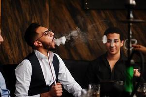 groep van knap retro goed gekleed Mens gangsters besteden tijd Bij club, roken hookah. multi-etnisch mannetje bachelor opleiding maffia partij in restaurant. foto