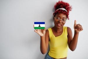 Afrikaanse vrouw met afro haar, slijtage geel singlet en bril, houden Lesotho vlag geïsoleerd Aan wit achtergrond, tonen duim omhoog. foto