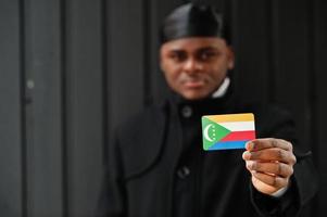 Afrikaanse Mens slijtage zwart durag houden comoren vlag Bij hand- geïsoleerd donker achtergrond. foto