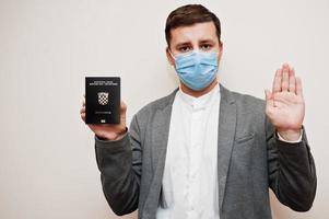 Europese Mens in formeel slijtage en gezicht masker, tonen Kroatië paspoort met hou op teken hand. coronavirus vergrendeling in Europa land concept. foto