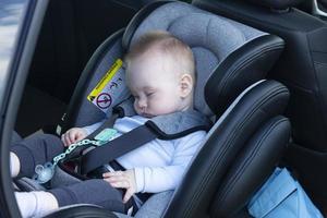 slapen jongen, een baby, zes maanden oud, is vastgebonden in een auto stoel in de passagier gedeelte. foto