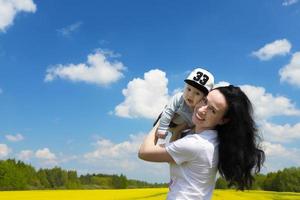 jong, mooi brunette, moeder, Holding haar weinig zoon in haar armen in een koolzaad veld, kopiëren ruimte. foto