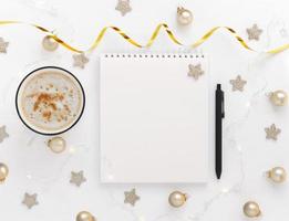 wit vel van notitieboekje met pen Aan wit tafel met kop van cacao of koffie, sterren, Kerstmis ballen en feestelijk guirlande. conceptuele planning, wens lijst voor de nieuw jaar foto