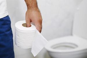 Mens lijdt van diarree hand- houden zakdoek papier rollen in voorkant van toilet schaal. constipatie in badkamer. behandeling maag pijn en hygiëne, Gezondheid zorg foto